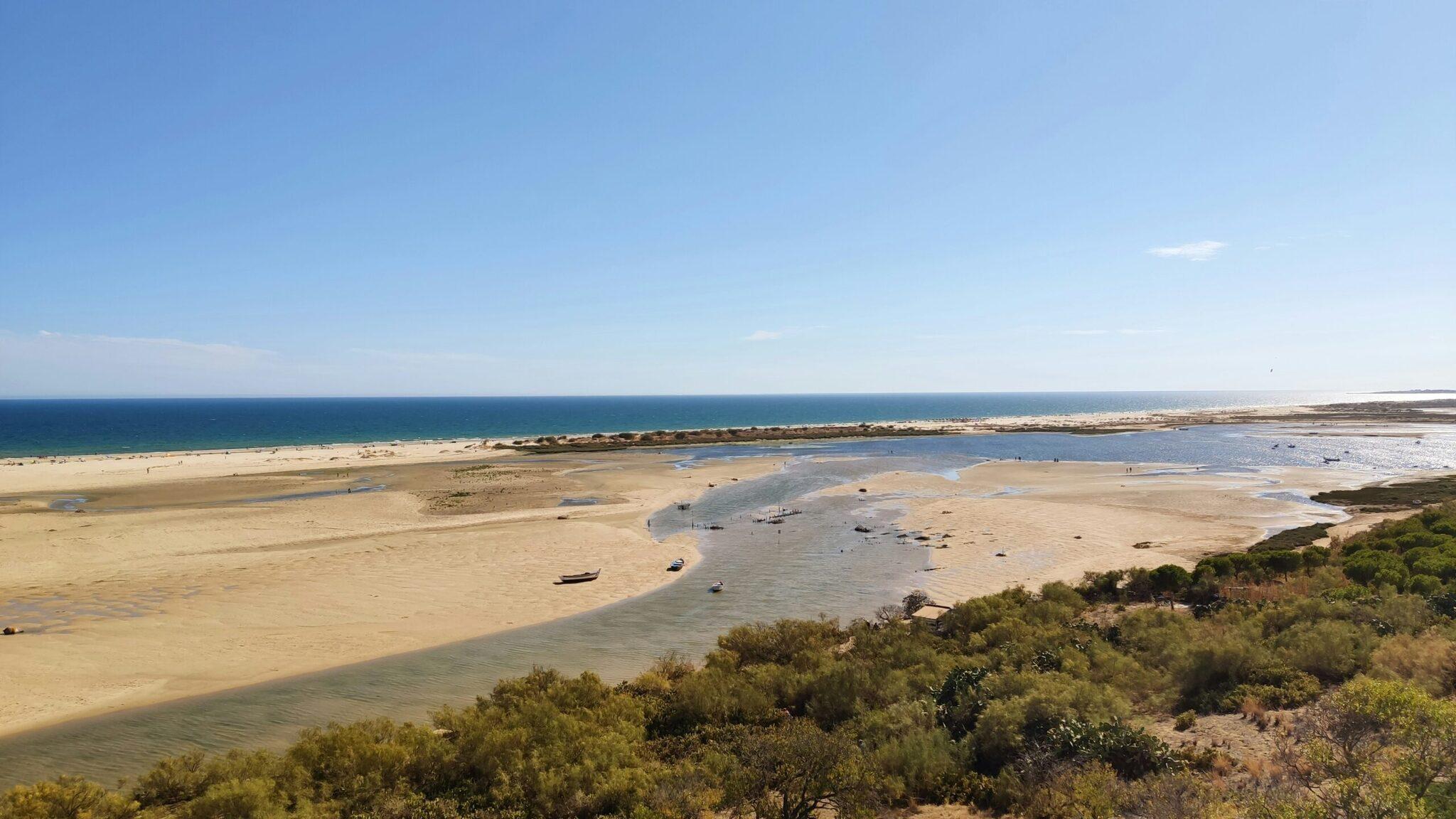Vue aérienne d’une baie côtière avec plage de sable, eau turquoise et bateaux amarrés par beau temps