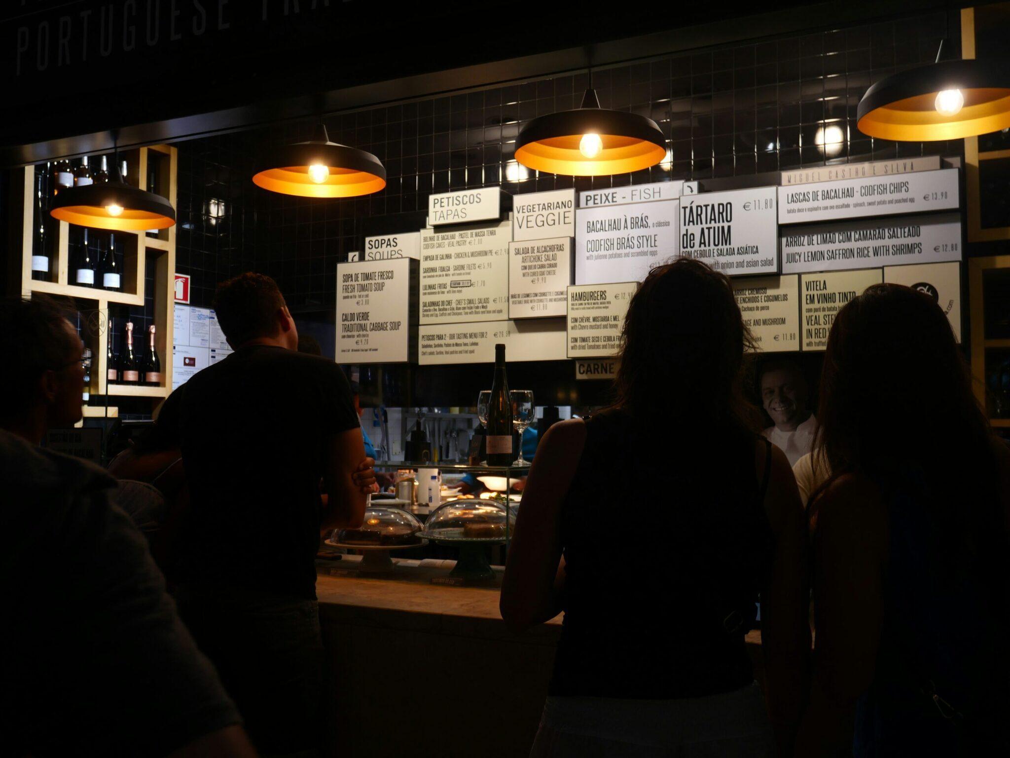 Une petite taverne portugaise de nuit avec menu affiché, clients au comptoir et luminaires dorés
