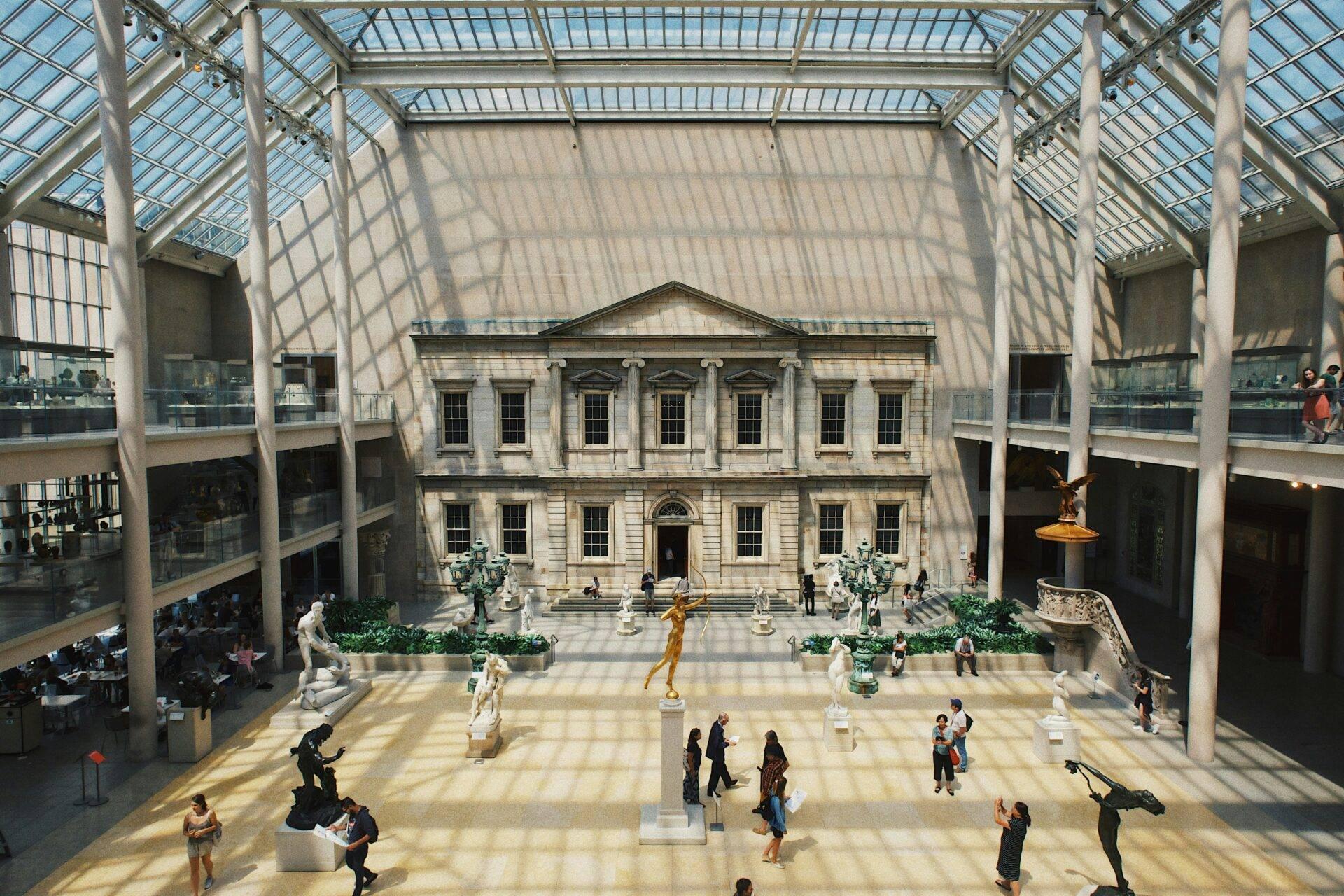 Un musée avec cour intérieure classique couverte de verre, visiteurs déambulant parmi des sculptures antiques
