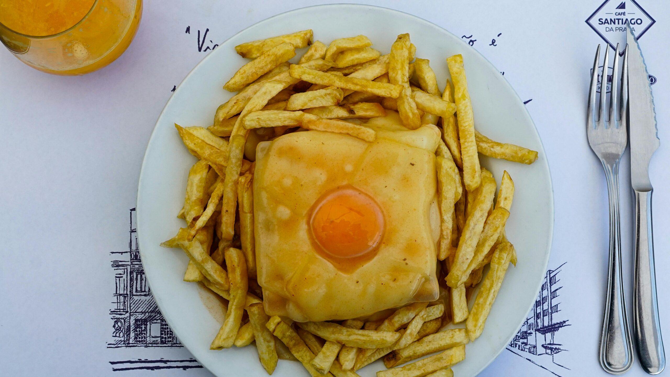 Un sandwich grillé au fromage garni d’un œuf, entouré de frites dorées, servi dans un restaurant portugais