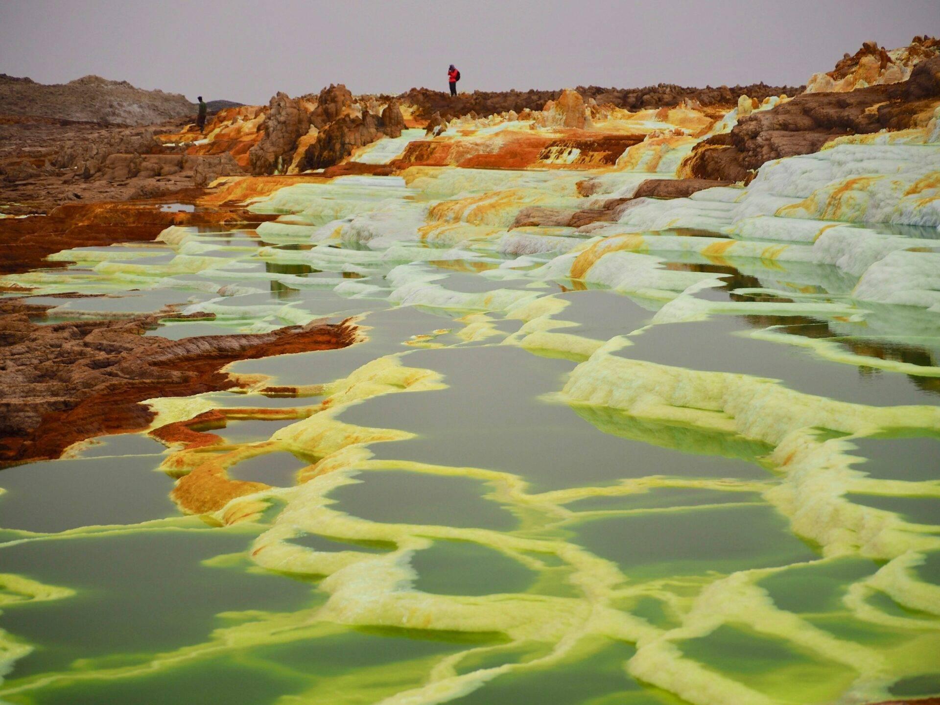 Bassins géothermiques aux eaux minérales colorées jaune et vert avec formations rocheuses orange et minérales
