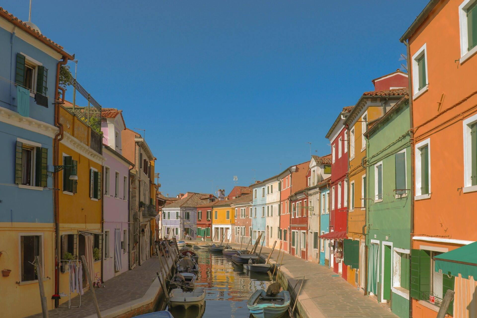 Une ruelle vénitienne colorée bordée de maisons jaunes, oranges et vertes avec des bateaux amarrés dans le canal