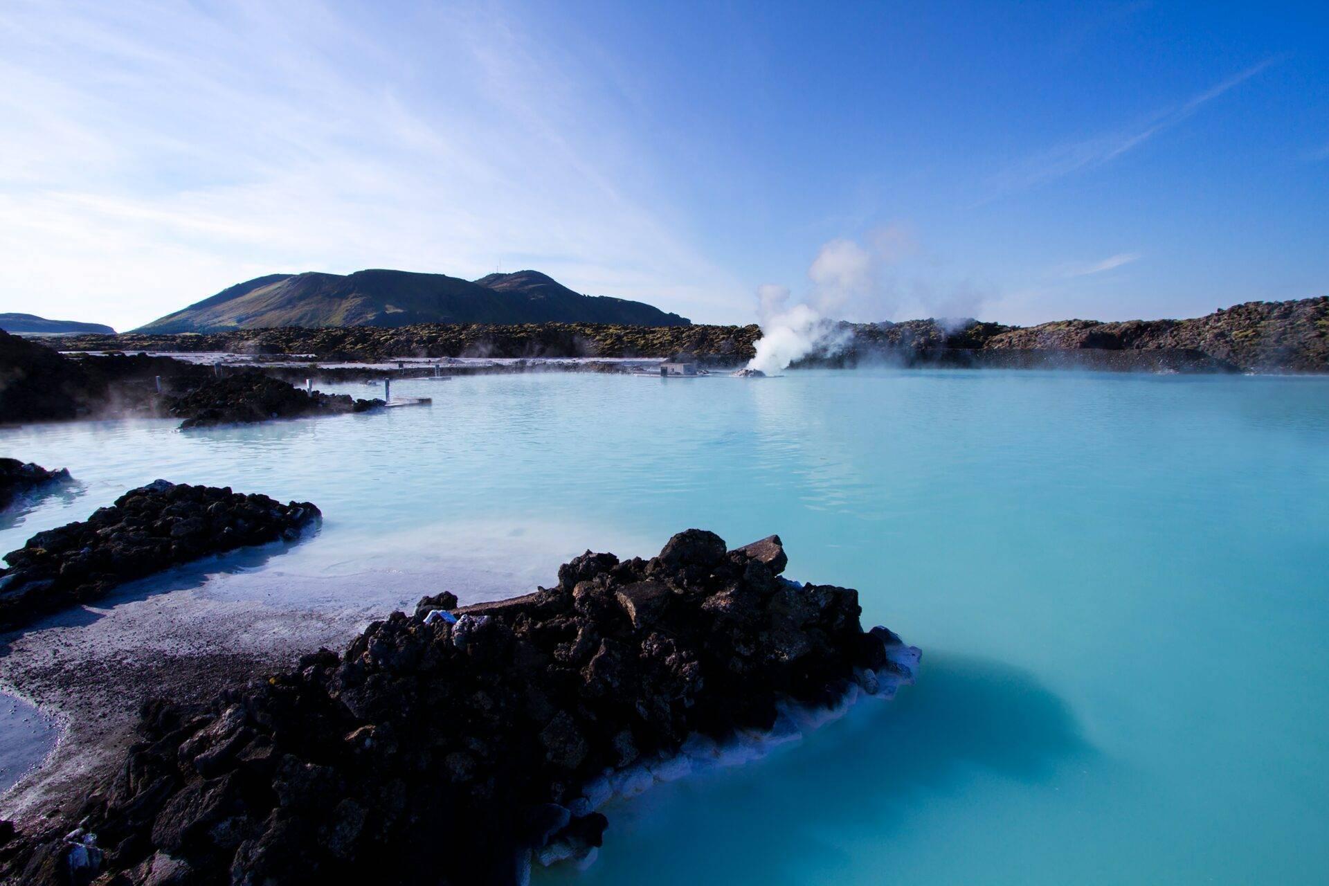 Lagon géothermique aux eaux turquoise entouré de roches volcaniques noires et de vapeurs chaudes